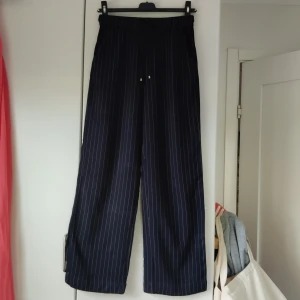 Vida byxor - Marinblå tunna och vida byxor med vita ränder. Gulddetaljer på snörena. Perfekt för svala sommarkvällar😊