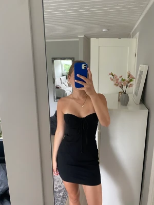 Svart klänning - Supersnygg bandeau-klänning med en snygg detalj som man ser på andra bilden! Endast använd en gång så i väldigt bra skick🤩
