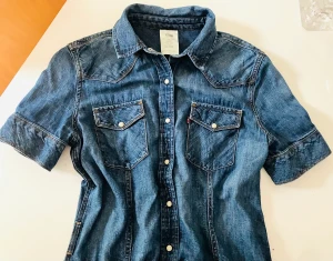 Levis Jeansklänning - Klassisk jeansklänning med stel krage, tryckknappar, detaljresår bak samt möjlighet till skärp/utan skärp. Passar som sommarklänning alt med stövlar på vinter.  Nypri 1599kr