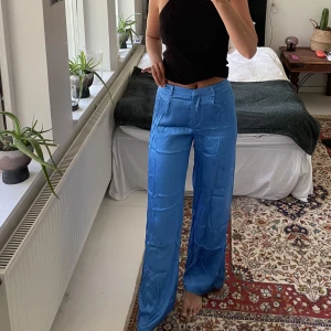 Blåa sidenliknande byxor - Säljer mina skönaste sideninspirerade byxor från Bershka. Använda för få gånger & legat i garderoben ett tag därav skrynkliga, enkelt att fixa! Storlek 32 men passar mig som normalt är 34-36 i byxor! Köparen står för frakten! Kram :-)