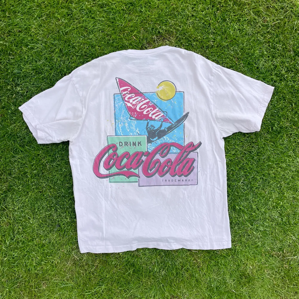 En t-shirt i en vit färg med svag nyans av rosa i. Coca cola tryck på bröstet samt ryggen, made in portugal. . T-shirts.