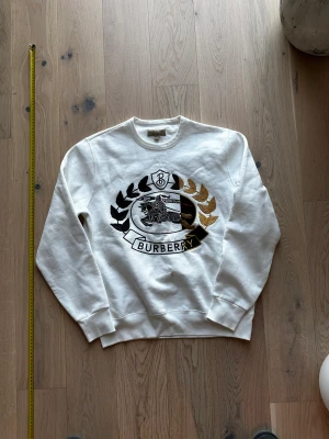 Burberry Crewneck Vit Storlek M - Vit Burberry Crewneck storlek M. Har lite små fläckar som kan gå bort vid tvätt. Sitter oversized. Retail 520$