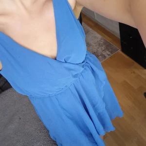 Blå Klänning (kortare framtill) - Tunt syntetiskt material, kortare fram släp baktill. Blå underkjol sydd under klänningen så ej genomskinlig. Stretchband i midjan.