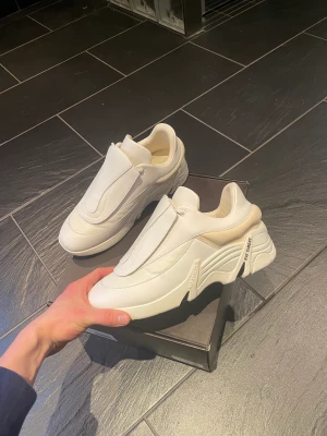 Raf Simons Skor - White Raf Simons Antei Leather Sneakers, Använda en gång! Kommer med original låda och lila  & vita pads som täcker skosnörena. Dessa går att byta och ta av helt! Har ni några mer frågor så skriv bara!