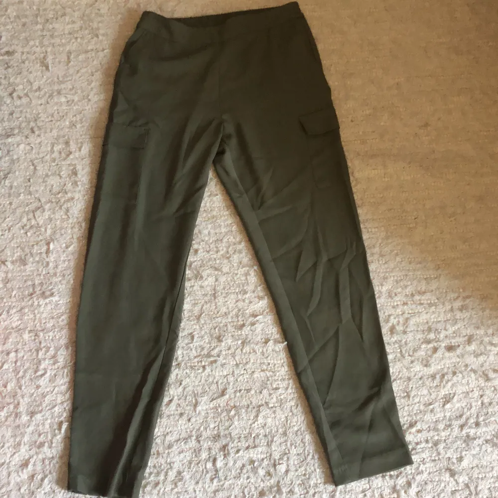 Militärgröna byxor med fickor på benen och resår i midjan . Jeans & Byxor.
