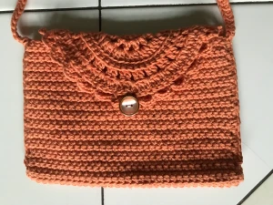 Virkad kuvert väska  - Handvirkad unik väska i mörkt aprikos färg. Spetsmönster på framsidan och en vacker knapp som den stängs med.  Mått: ca 20x13 cm  Passar lagom till mobilen och något mer.  Kan beställas likadan i de flesta färger. Tar Max 1vecka. 