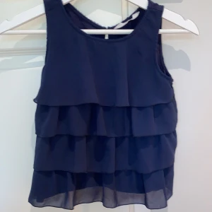 Blus med volanger - Denna jätte fina marinblå blusen från HM:s barnavdelning. Vid nacken så är det ”lösa trådar”, men det är inget man tänker på (3:dje bilden. Tröjan passar för 146 och 152. Kontakta för mer bilder och info. KÖPAREN STÅR FÖR FRAKTEN!