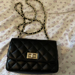 Väska liten - Mindre svart axelbandsväska med gulddetaljer. Har haft den ett tag men är i fint skick.