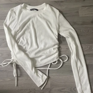 Zara långärmad tröja - Säljer denna fina tröjan från Zara då den inte kommer till användning💗. Vit långärmad tajt passform, med snören på sidorna som man kan justera själv. Aldrig använd!