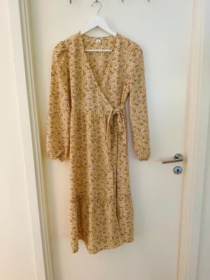 Gulblommig långklänning - Gulblommig långklänning i omlottmodell från Monki. I fint skick, som ny. Storlek 36.