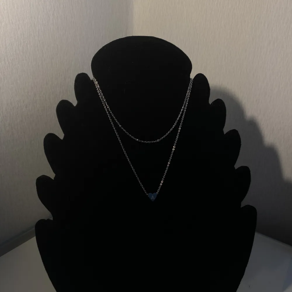 Ett halsband med bokstaven A. De är ett dubbel halsband med lite små pärlor på. Accessoarer.