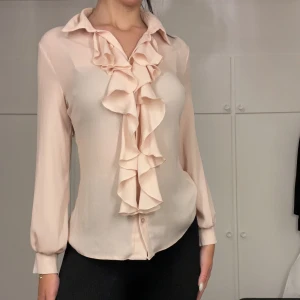 Blus med volanger  - Blus med volanger i rosa färg. Blusen är i storlek 38 och har en mycket smickrande passform. Den är dessutom i bra skick.