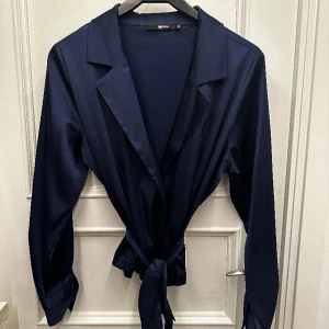 Blus med knytning - Mörkblå blus med knytning från Bikbok. Saknas en knapp på armen på ena sidan. Se sista bild. Annars fint skick. 