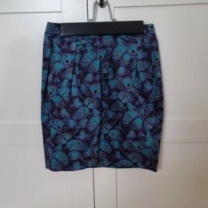 Snygg kjol med påfågel mönster - Snygg kjol i bra kvalité med påfågel mönster. Kjolen går att använda till vardags som till fest beroende på övrig kombination. Den är i stl.36 och sitter åt högt vid midjan och inte ner vid höften. Se bild. Nypris 1år sedan 800:-. Sparsamt använd.