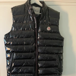 Monclerväst - Säljer denna trendiga Monclerväst, svart med röda & vita detaljer. Passar bra nu mot våren samt sommaren. Den är liten i storleken, skulle säga att den är en M. 1000 kr + frakt. 