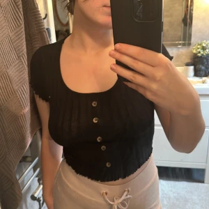 Svart t-Shirt med knappar - De är en kortare svart T-shirt med knappar från New Yorker. Den är i storleken S.