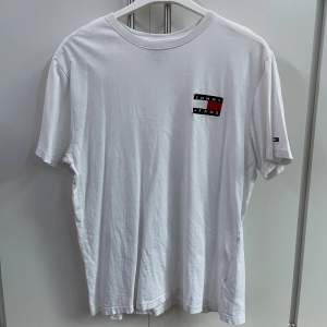 Vit Tommy Hilfiger t-shirt i storlek XL men passar som L, broderad logga på bröstet. Bra skick förutom två hål vid loggan på bröstet (se bild tre). 