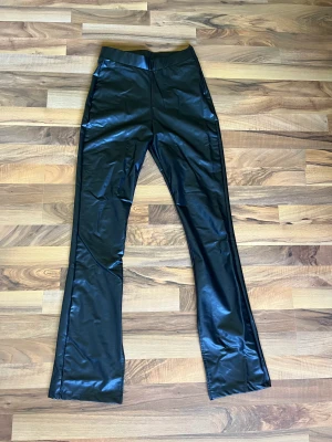 Byxor med läderlook - Svarta, tretchigabyxor med hög midja. Finns dragkedja på sidan och snygga slitsar på insidan av benen. Använd fåtal gånger, fint skick.
