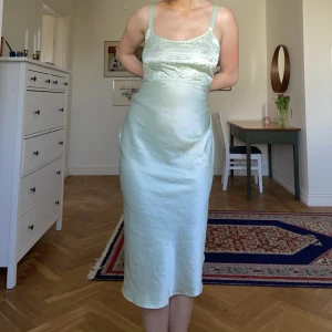 Ljusgrön satinklänning - Sitter tajt i midjan, vidare nedtill. Okänt märke. Köpt vintage. 