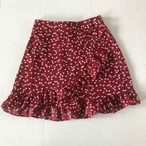Kjol  - En röd kjol med hjärtan på från shein. Kjolen har volang och har en dragkedja i sidan. Storlek xs! Säljer för 59kr, använd 2 gånger så fint skick. Köparen står för frakten💖
