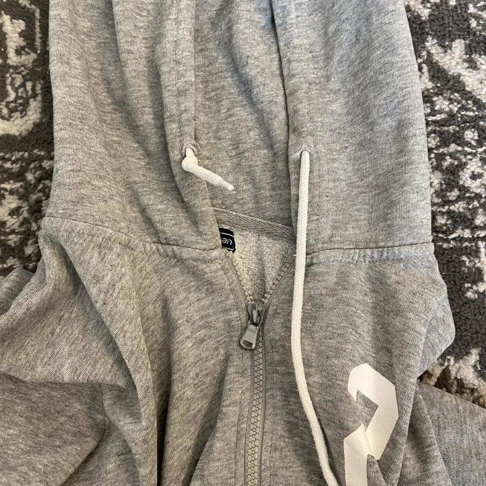 En grå zip up hoodie med ett tryck på och vita snören. Älskar den men kommer inte till användning💌. Tröjor & Koftor.