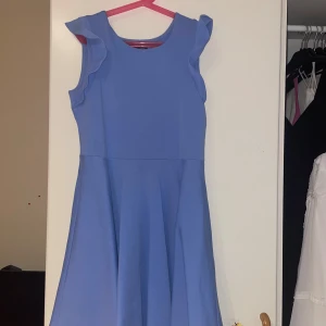 Blå klänning från Ralph Lauren - Säljer en superfin blå klänning från Ralph Lauren. Den har en enkel och elegant design med ärmlös stil och volangdetaljer vid axlarna. Perfekt för både vardag och fest!