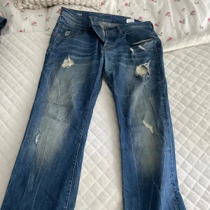 Blå slitna jeans - Säljer ett par blå jeans med slitningar på framsidan. De har en klassisk femficksdesign och en snygg tvätt som ger dem en cool, avslappnad look. Perfekta för en casual outfit!