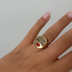 Guldfärgad ring med ansikte-design - Supercool ring i guldfärg med en glad ansikte-design. Perfekt för att ge lite humor och stil till din outfit! Köpt för 2 år sen på Arket, är i perfekt skick. 