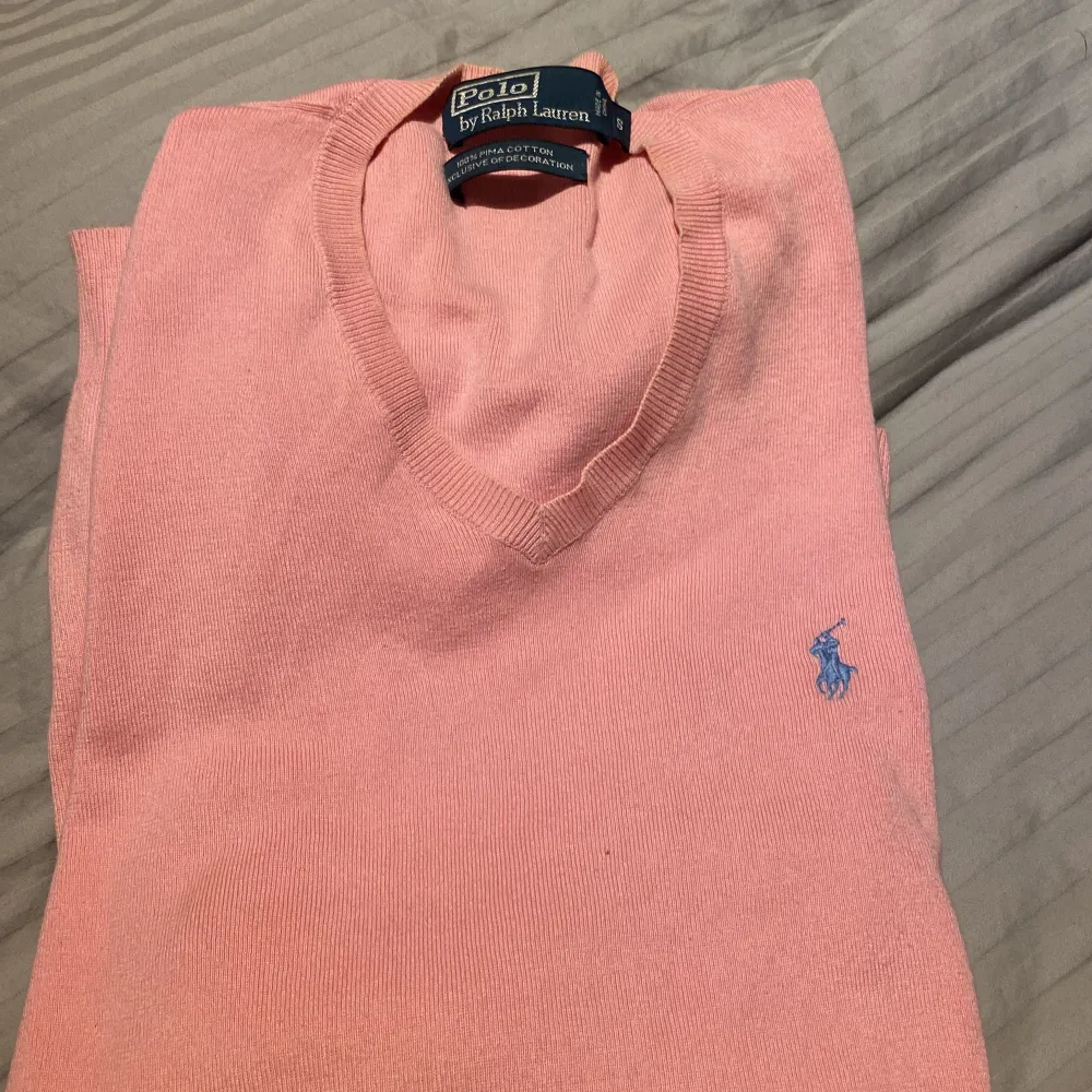 Säljer en snygg rosa tröja från Polo Ralph Lauren i storlek S. Den är gjord av 100% Pima bomull vilket gör den supermjuk och skön att ha på sig. Tröjan har en klassisk v-ringning och det ikoniska blåa Polo-loggan broderad på bröstet. Perfekt för både vår och höst!. Tröjor & Koftor.