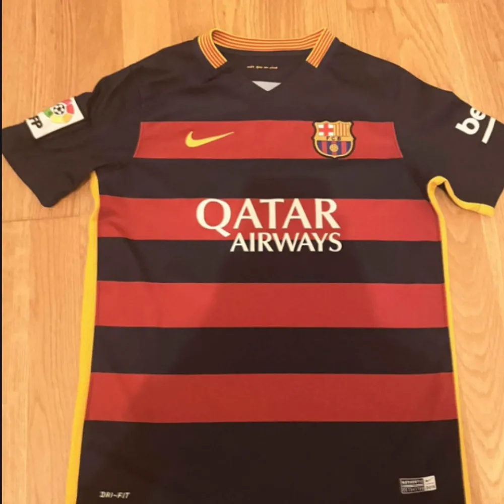 Säljer en äkta FC Barcelona fotbollströja från 2015. Den är i mörkblått med röda horisontella ränder och gula detaljer. Tröjan har korta ärmar och är i Dri-FIT material för bästa komfort. Perfekt för alla Barca-fans! 💙❤️. T-shirts.