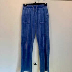 Blå velourbyxor med fickor - Säljer ett par snygga blå velourbyxor från Juicy couture, bred resår i midjan och snörning. Byxorna har stora fickor både fram och bak, vilket ger en cool och avslappnad look. Perfekta för en chill dag hemma. Supermjuka och bekväma!