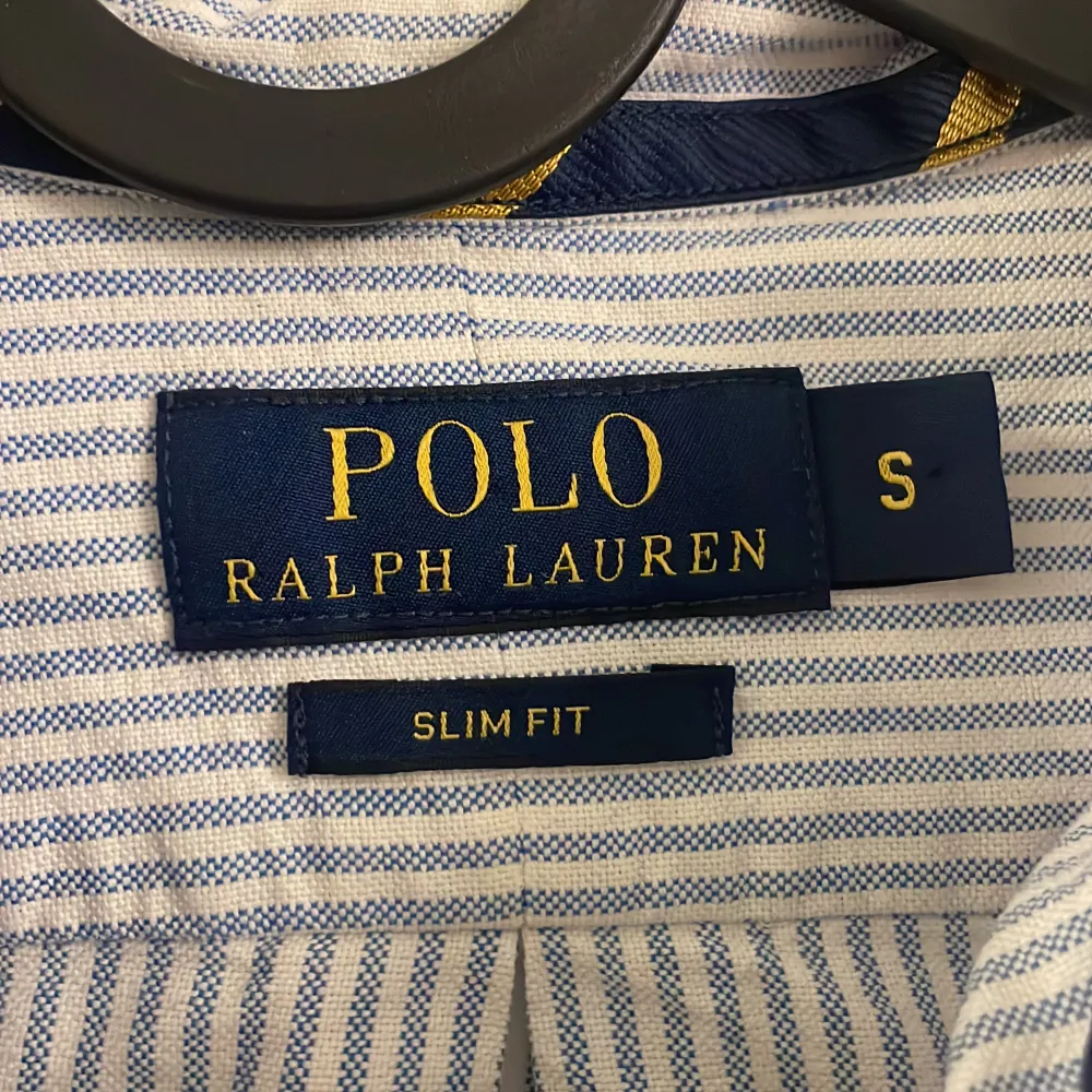 Säljer en stilren och klassisk randig skjorta från Polo Ralph Lauren. Den är i en snygg blå och vit färgkombination med långa ärmar och knappar framtill. Skjortan är i slim fit och har den ikoniska broderade loggan på bröstet. Perfekt för både vardag och fest!. Skjortor.