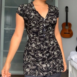 Svart blommig klänning från Sisters Point - Säljer en superfin svart klänning från Sisters Point med ett blommigt mönster i vitt. Klänningen har korta ärmar och en v-ringad hals. Den är perfekt för både vardag och fest! 💐