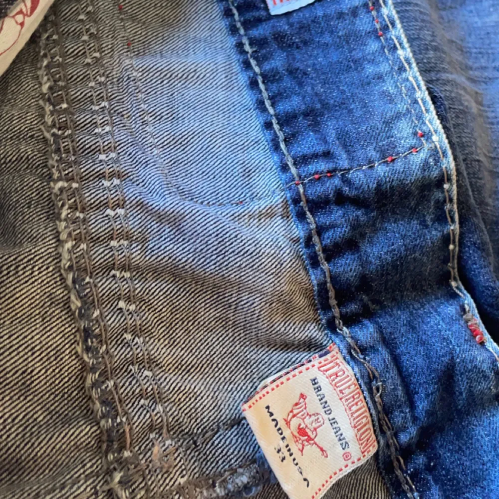 Säljer ett par snygga True Religion jeans i storlek 33. De är i en klassisk blå färg med coola slitningar och kontrastsömmar. Jeansen har en normal passform och är tillverkade i 100% bomull, vilket gör dem både bekväma och hållbara. . Jeans & Byxor.