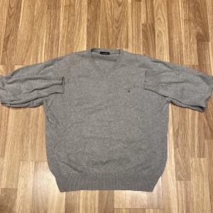 Grå v-ringad tröja från Tommy Hilfiger - Säljer en stilren grå v-ringad tröja från Gant. Den är i 100% bomull vilket gör den supermjuk och bekväm. Perfekt för både höst och vår! Tröjan har en liten broderad logga på bröstet och ribbade muddar vid ärmslut och nederkant. 