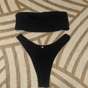 Svart bikini från Junkyard - Säljer en svart bikini från Junkyard i storlek M. Den har en enkel och modern design med en bandeau-topp och matchande trosa. Perfekt för sommarens alla badäventyr! 🖤