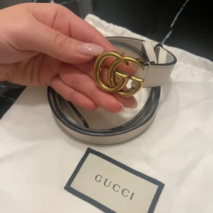 Vit GG Marmont Thin Belt från Gucci - Säljer ett stilrent och elegant vitt bälte från Gucci, modellen GG Marmont Thin Belt. Bältet har en dubbel G-spänne i guld och är tillverkat i skinn. Size 70 och är 2cm i bredd. Skärpet är i nyskick 
