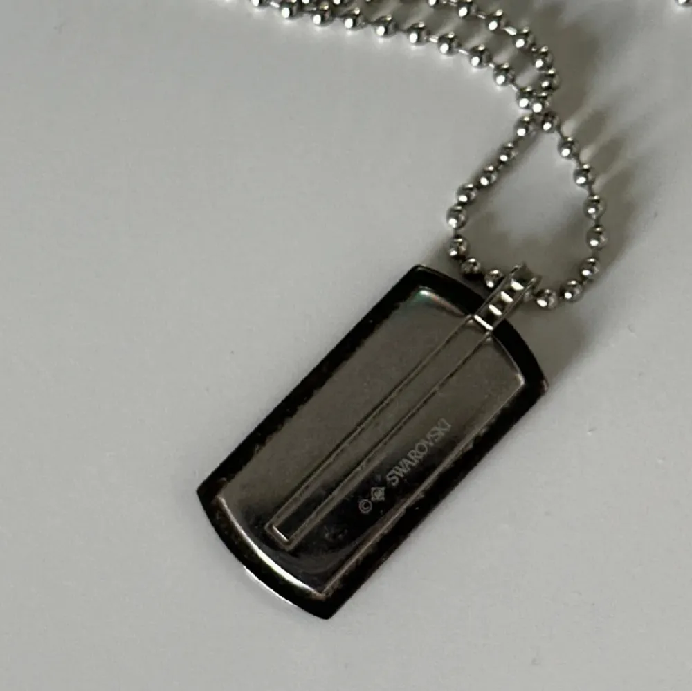 Säljer ett stilrent Swarovski silverfärgat halsband med en rektangulär bricka. Kedjan är av kulmodell och brickan har en enkel design. Perfekt för en minimalistisk look eller som en personlig accessoar.. Asusteet.