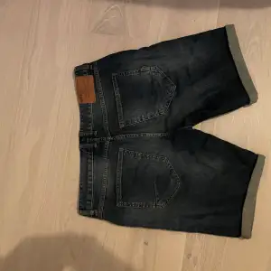 Säljer ett par snygga mörkblå jeansshorts från Jack & Jones. De har en klassisk femficksdesign och är i bra skick. Perfekta för sommaren med en casual look. Shortsen har en knapp och dragkedja framtill.