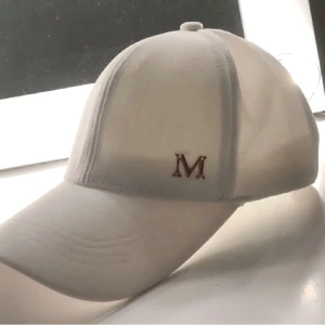 Vit keps med bokstaven M - Säljer en stilren vit keps med en snygg broderad bokstav 'M' i guld på framsidan. Perfekt för sommardagar eller som en cool accessoar till din outfit. Kepsen har en klassisk design med en böjd skärm och justerbar passform.