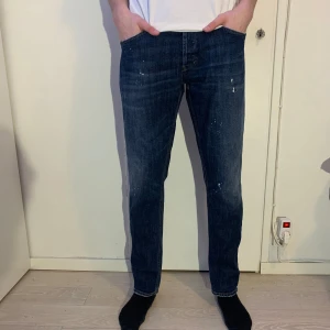 Mörkblå Dondup jeans  - Vi säljer ett par mörkblå jeans från Dondup i modellen George som är slim. Jeansen har lite paint splash vilket är en del av designen. Modellen är 184 cm och väger 69 kg.