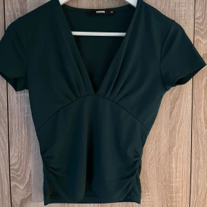 Mörkgrön topp från BikBok - Snygg mörkgrön topp från BikBok med v-ringning och korta ärmar. Toppen har en figurnära passform och är tillverkad i ett mjukt material.