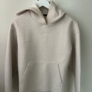 Beige ribbad hoodie - Säljer en stilren beige ribbad hoodie med en stor ficka framtill. Perfekt för en avslappnad look. Den har långa ärmar och en bekväm huva.