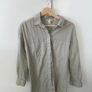 Grön lång linneskjorta från H&M - Grön skjorta i linneblandning från H&M. Skjortan har långa ärmar är lite längre modell. Använd men i utmärkt skick!