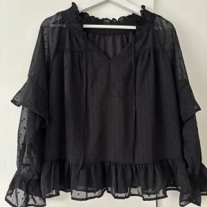 Svart blus med volanger  - En svart blus med V-ringning samt knytning 🩷Blusen har dubbelt tyg både fram och bak, medan ärmarna har ett genomskinligt tyg med en volang 😇Endast testat!