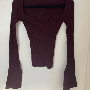 Vinröd ribbad topp från H&M - Säljer en snygg vinröd ribbad topp från H&M. Toppen har en v-ringad design och långa ärmar, perfekt för en stilren look. Passar bra till både jeans och kjol. Perfekt för höst och vinter!