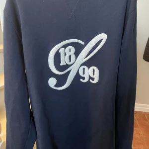 Mörkblå tröja från Stenströms - Säljer en stilren mörkblå tröja från Stenströms med ett broderat '1899' i vit på framsidan. Tröjan har långa ärmar och en klassisk passform. Perfekt för en avslappnad men ändå elegant look. Tröjan är i nyskick. Använd max 2 gånger. Köpt för 1499. Säljer den för 900 