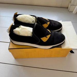 Fendi Monster Eye Slip On (st 43) - Storlek 43. Snygga svarta sneakers från Fendi med unika gula detaljer och silverfärgade nitar på hälen. Inköpta i Beverly Hills av mig, finns kvitto med mitt namn på.
