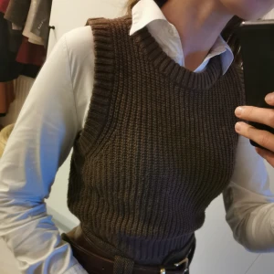 Brun stickad väst Slipover - Säljer en snygg brun stickad väst/slipover med ribbad design från Hm. Perfekt för lager-på-lager-stil och ger det där lilla extra till din outfit. Passar bra över en skjorta eller blus. Längd: 43cm. Bredd: 32 cm. Storlek S men passar även M. 