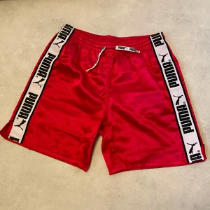 Rosa shorts från Puma - Coola retro shorts från Puma i mörk rosa färg. Skönt glansigt material, liten skada i grenen, annars i bra skick! Storlek 164, motsvarande XS